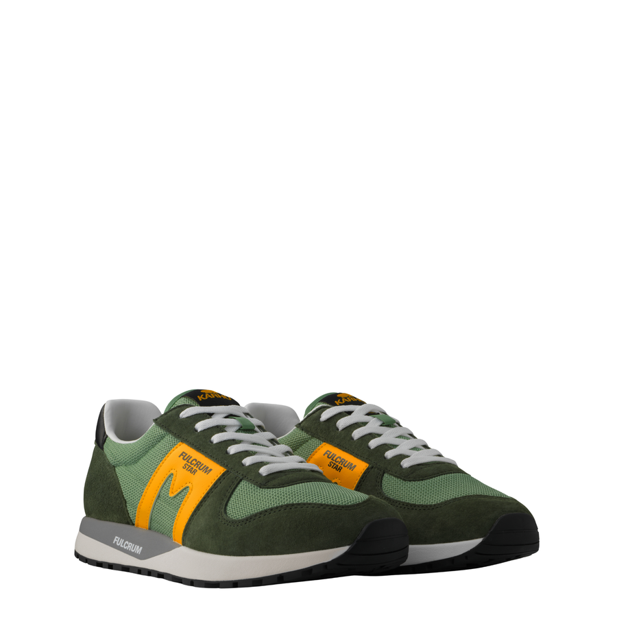 A low-top Karhu Fulcrum Star sneaker, featuring a green mesh and suede upper with a prominent mustard yellow 'M' logo on the side, white laces, and a gray and white midsole.