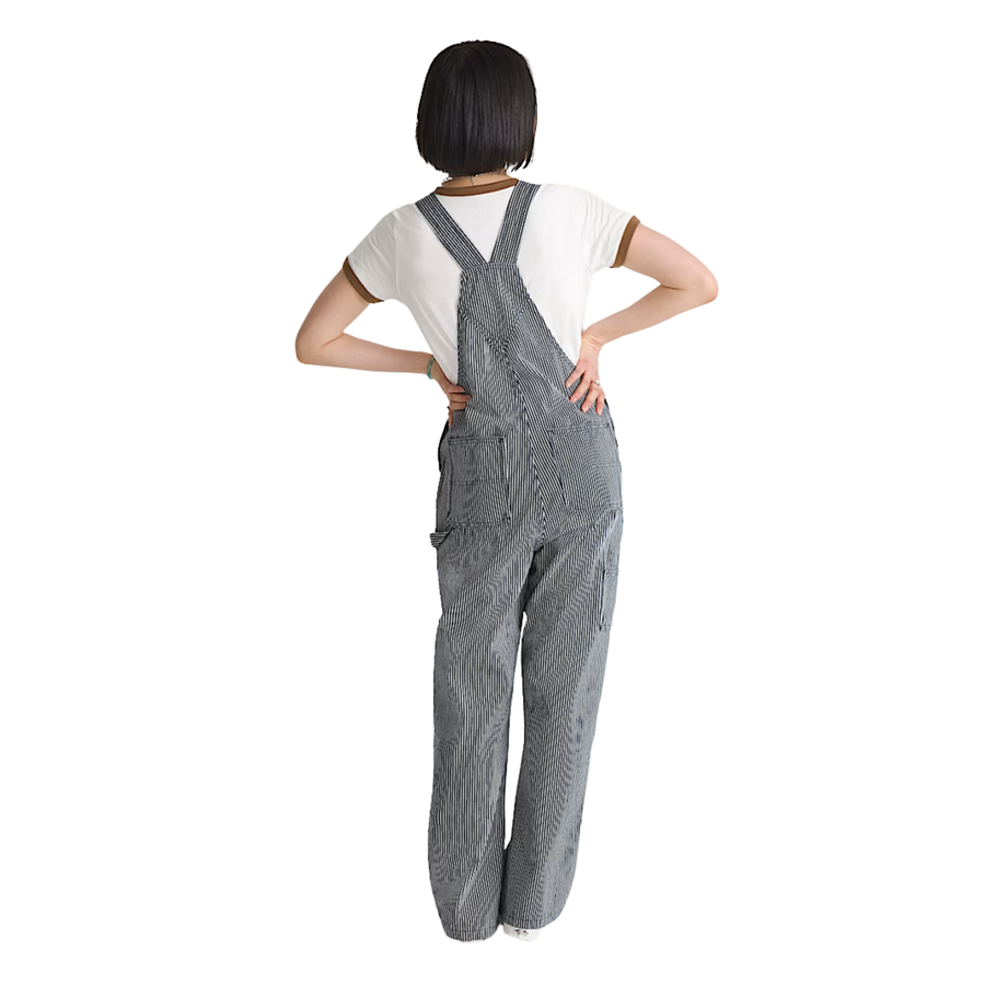 A woman modeling gray and white vans chore stripe vertically striped work overalls over a white t-shirt, standing against a plain white background.