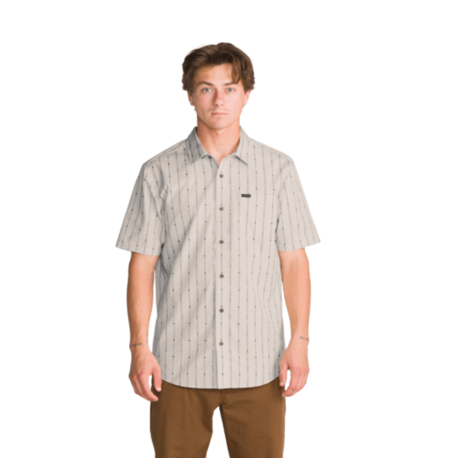 a man wearing an off white volcom bankstone ii short sleeve button-up shirt with vertical pattern with brown pants on a white background
