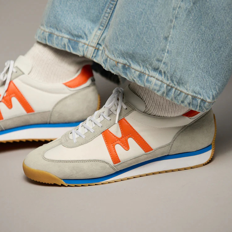 White karhu mestari 76 sneaker with orange 'M' logo on a white background