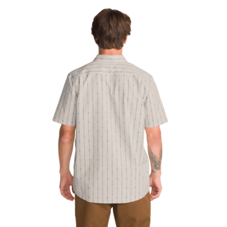 a man wearing an off white volcom bankstone ii short sleeve button-up shirt with vertical pattern with brown pants on a white background