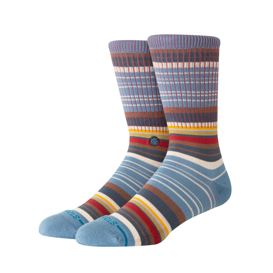 A pair of stance jorongo pop crew socks with a multicolor striped pattern featuring shades of blue, brown, red, yellow, and white, displayed against a plain white background.