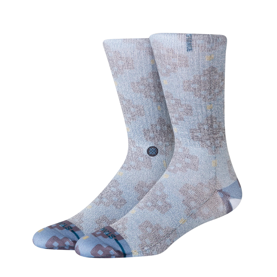 A pair of Stance alhambra butterblend crew socks in a light blue-gray colorway with a distressed brown tree pattern and small yellow accents, shown on a plain white background.