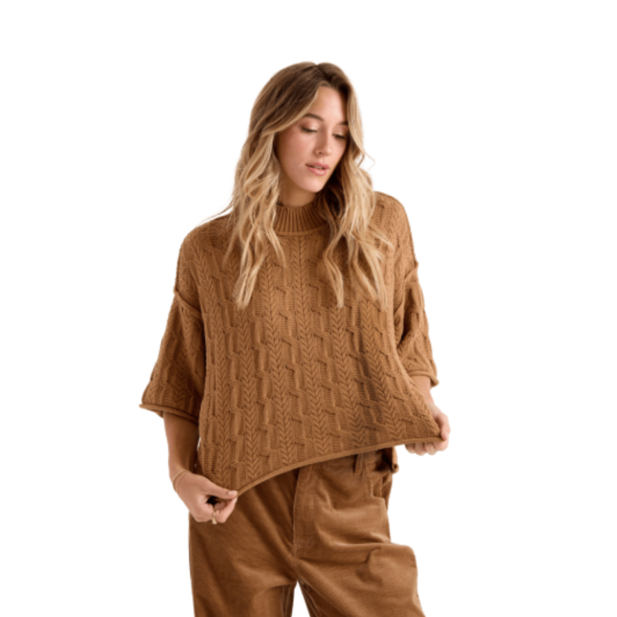 A woman wearing a brown volcom oversized cable-knit mock-neck sweater and matching brown corduroy pants, shown against a plain white background.