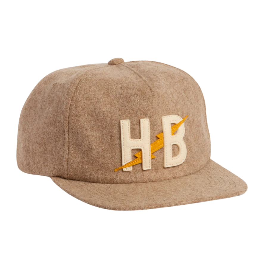 A flat-brim howler brothers snapback cap in a heathered tan wool-like fabric, featuring a prominent embroidered 'HB' logo in cream with a yellow lightning bolt detail on the front.