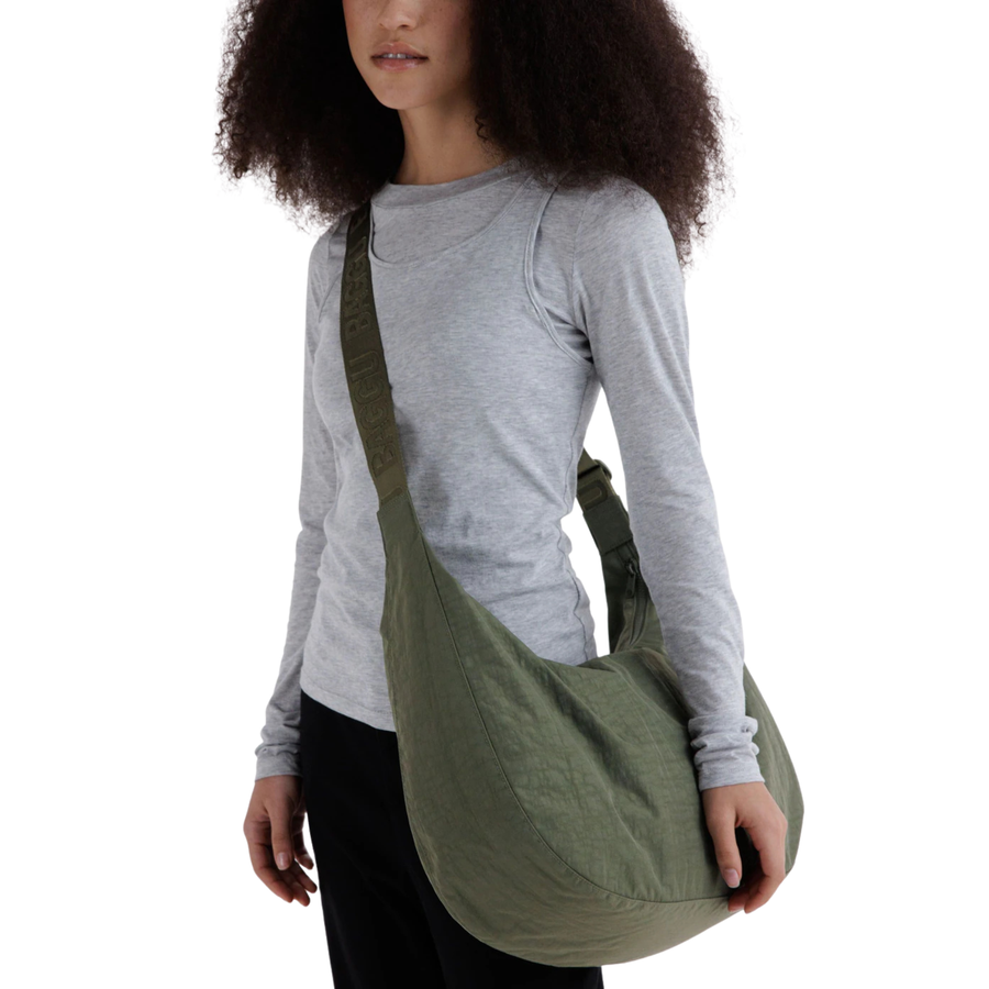 An olive green baggu crescent-shaped shoulder bag with a single strap and a small hanging tag, shown against a plain white background.