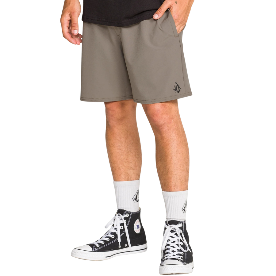 Man wearing a black tank top and TAN volcom nomaly elastic waist shorts on a white background
