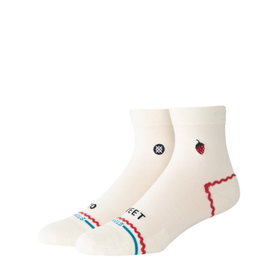 A pair of Stance crew socks in off-white, featuring a black circular logo with a white cross on the front ankle, a small red strawberry graphic on the side, and red and blue wavy stripe accents near the toe.