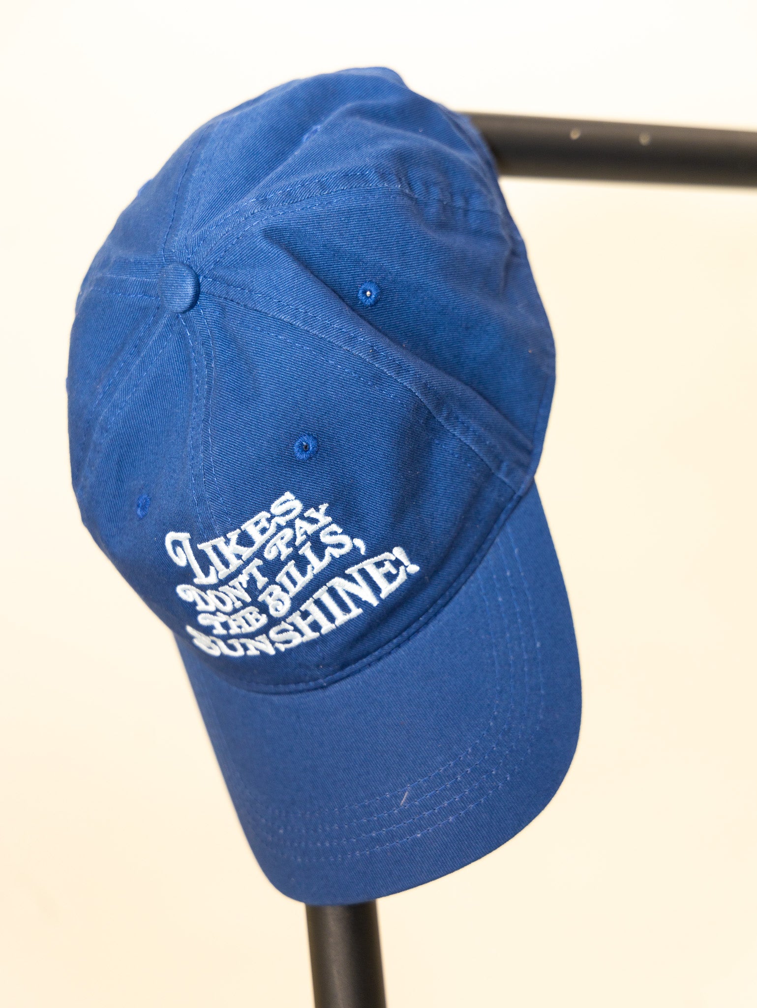 blue embroidered hat with the phrase likes don't pay the bills sunshine