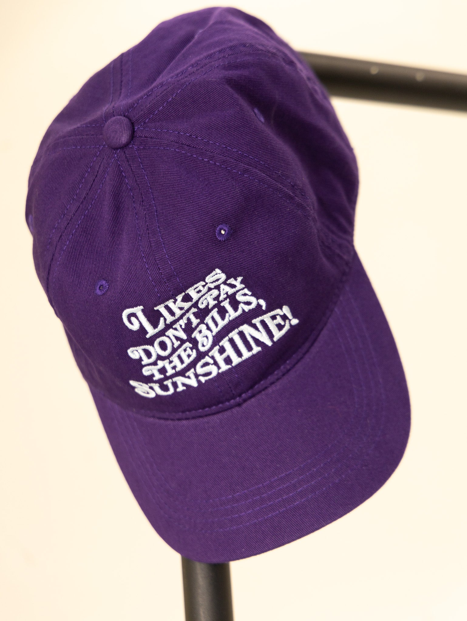 purple embroidered hat with the phrase likes don't pay the bills sunshine