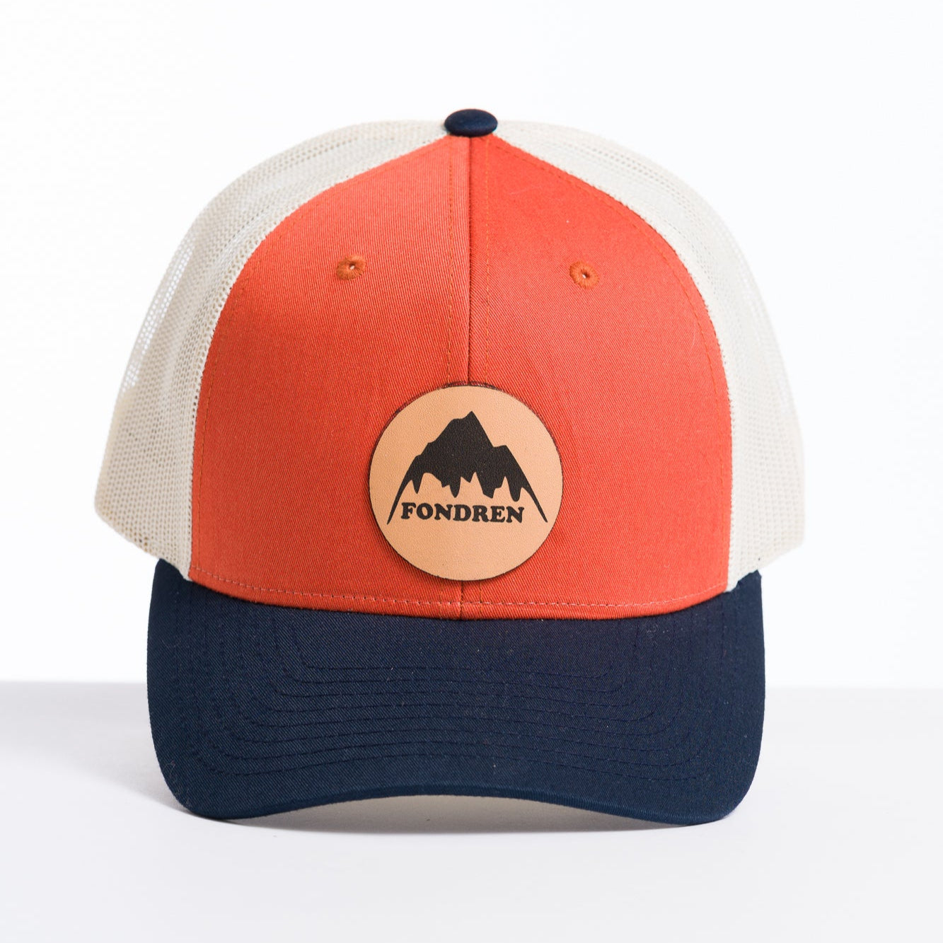 Trucker hat with navy bill, orange front panel and white back with a leather circle patch with the words fondren and a picture of a mountain