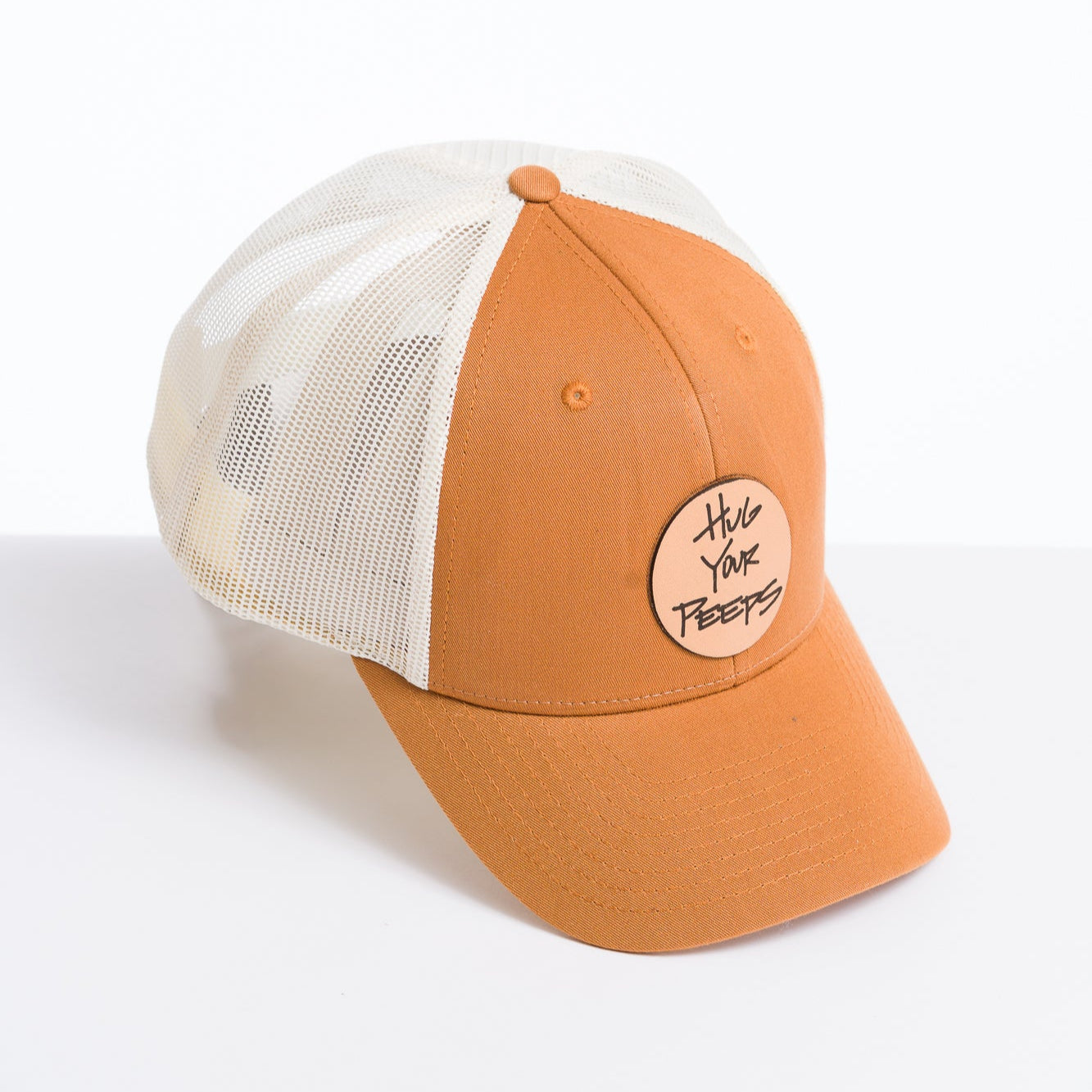 orange and white trucker hat with a hug your peeps leather patch on the front panel