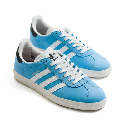 baby blue adidas gazella skate shoes in collaboration with famila skate shop and mnufc with white stripes and a white sole