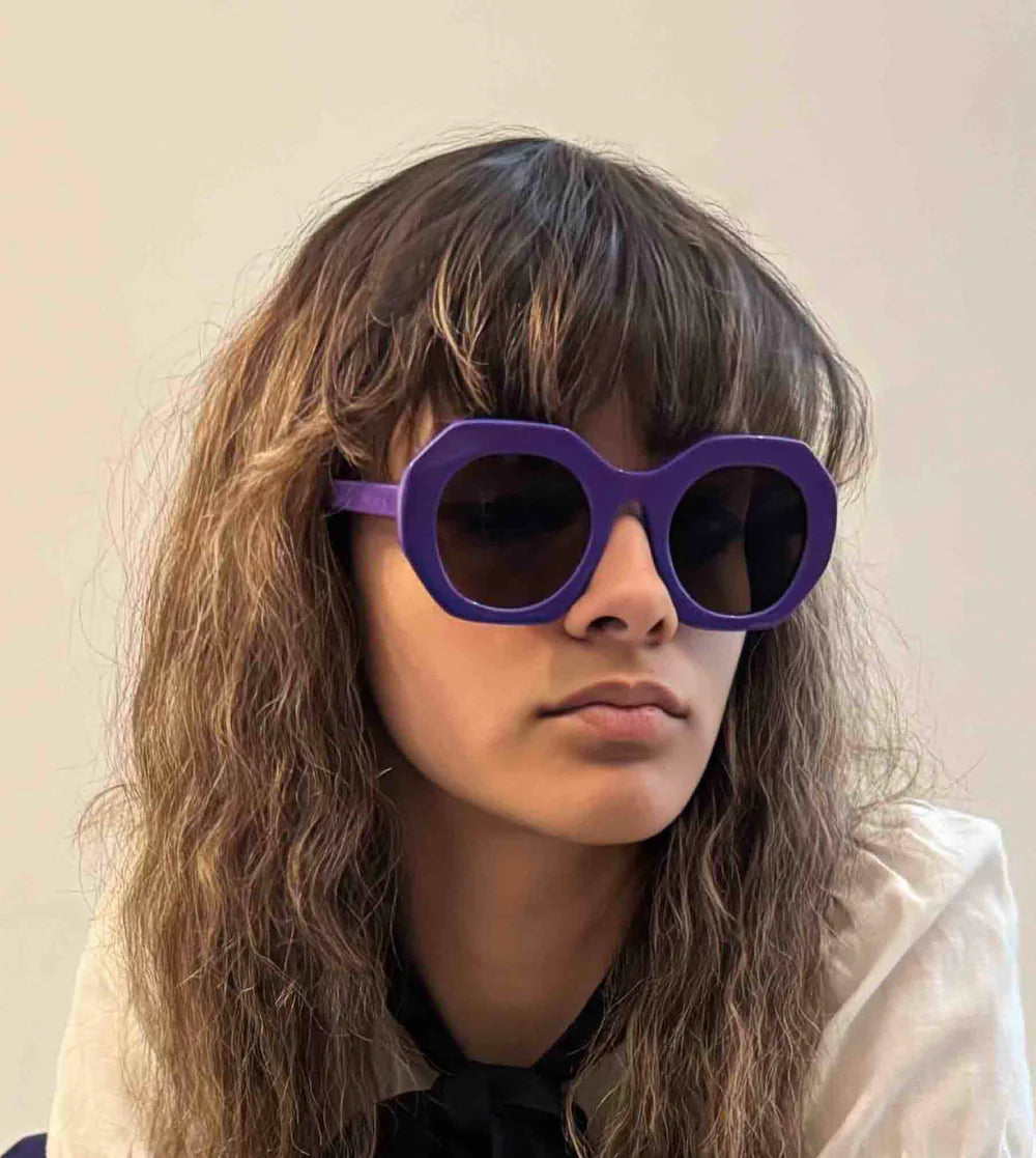 Person wearing large purple sunglasses with a neutral background Purple spitfire sunglasses with brown lenses on a white background