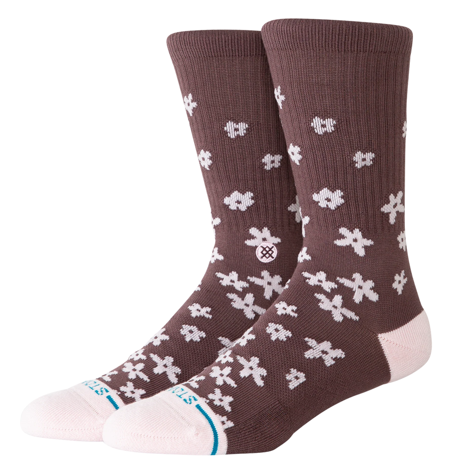 A pair of Stance crew socks in a dark brown color, featuring a white pixelated snowflake pattern and a light pink toe and heel, with the Stance brand logo visible on the side and toe.