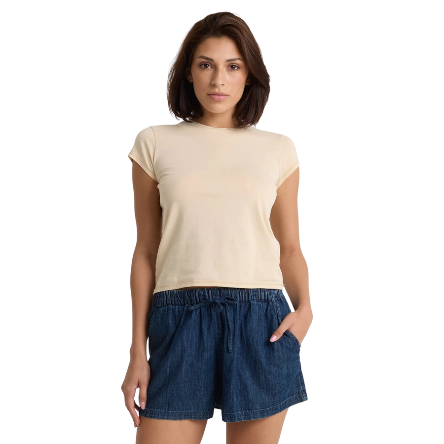 Woman wearing a beige volcom lived in stone wash t-shirt and blue shorts on a white background