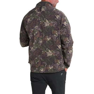 a man wearing A long-sleeve quarter-zip howler brothers pullover fleece, featuring a dark green and brown tropical leaf camouflage pattern. It has a black chest pocket with a white and red Howler logo patch, a stand-up collar, and zippered hand pockets.