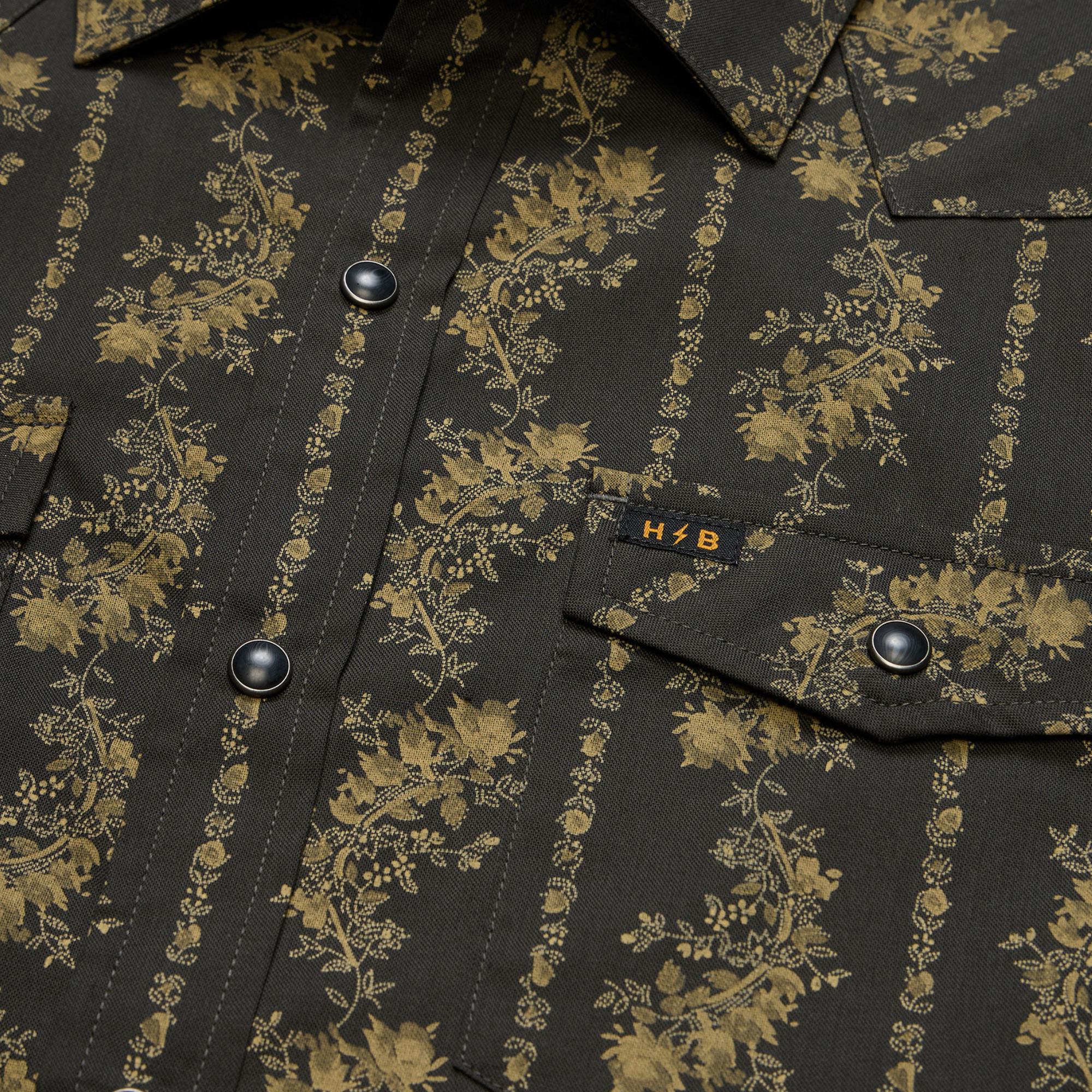 close up of a Holwer Brothers H Bar B Snapshirt grampa's curtains in a black with a gold floral design on a white background