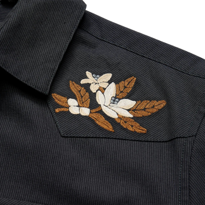 close up of a howler dark navy western-style button-up shirt with embroidered eagle details on the shoulders and beige pants, photographed against a plain white background.