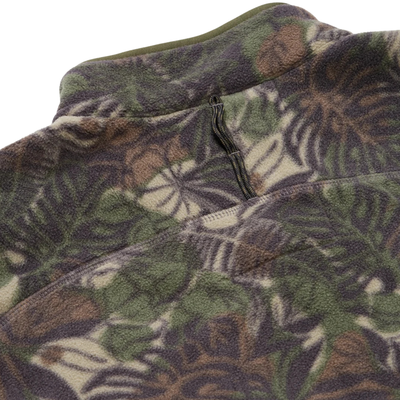 close up of A long-sleeve quarter-zip howler brothers pullover fleece, featuring a dark green and brown tropical leaf camouflage pattern. It has a black chest pocket with a white and red Howler logo patch, a stand-up collar, and zippered hand pockets.
