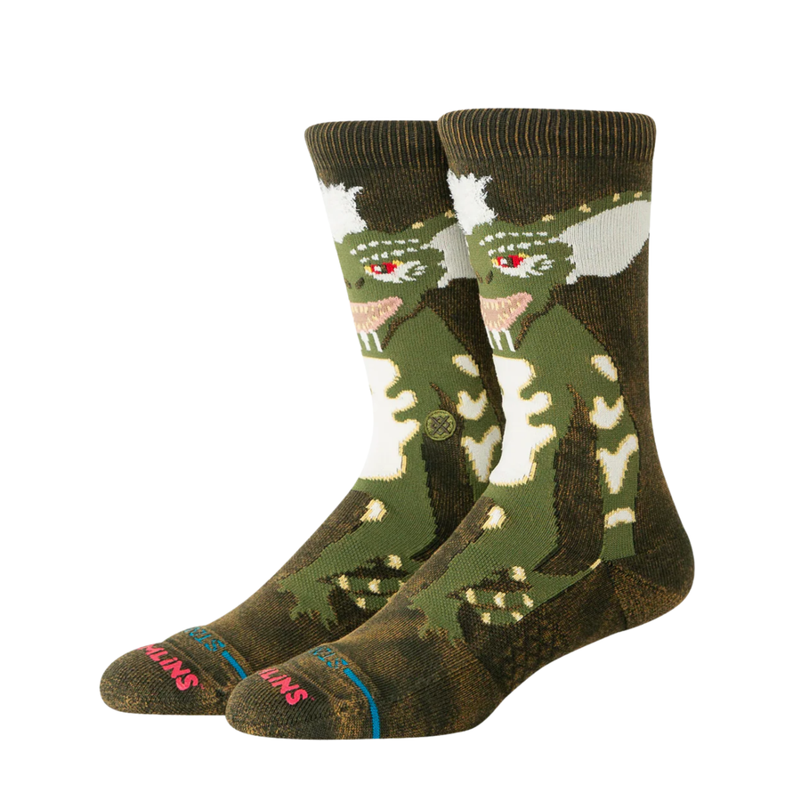 A pair of stance gremlins crew socks featuring a green and brown stripe from gremlins design on the upper leg, red eyes, and 'stance' printed in red on the toes.