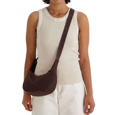 Person wearing a brown baggu small crescent nylon shoulder bag on a white background