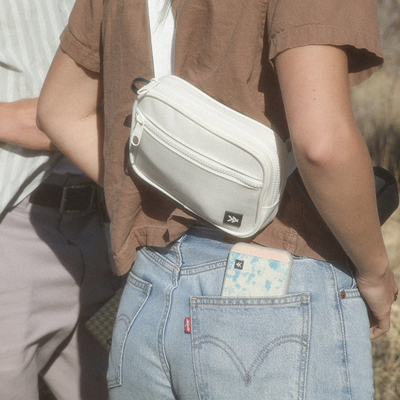 Person wearing a white waist bag with a visible brand logo, standing outdoors.