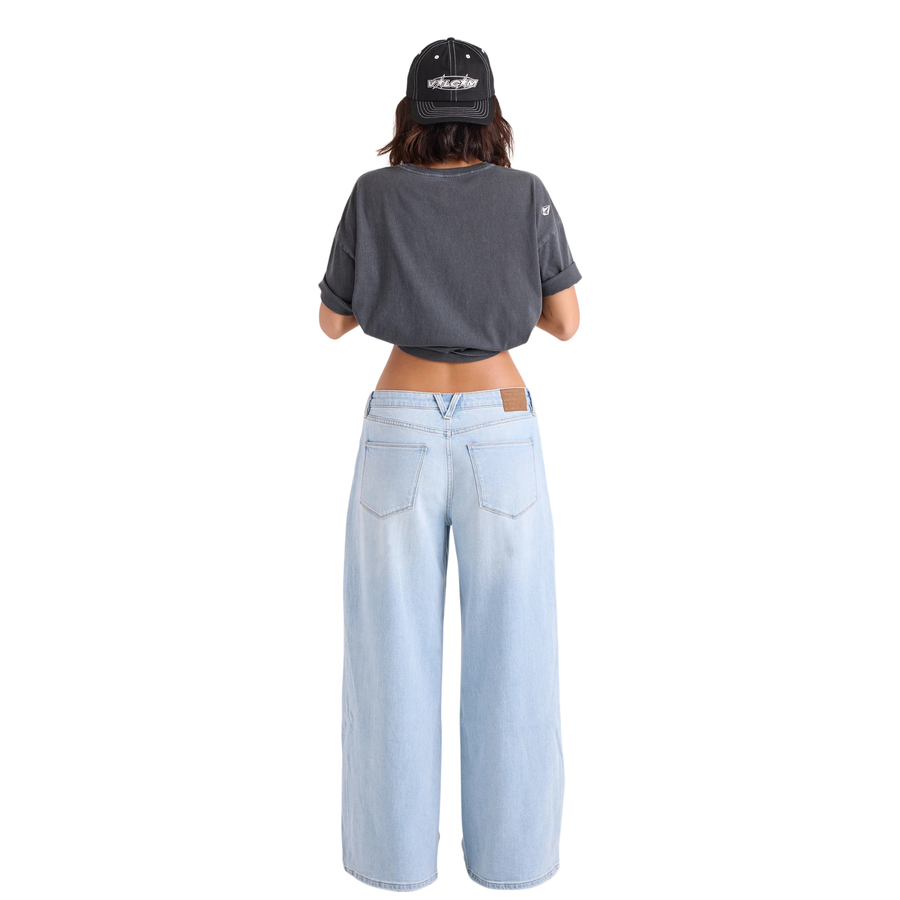 A woman in a black hat and black tee shirt wearing volcom stoned boyfriend low rise jeans on a white background