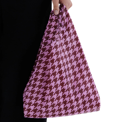 A pink and dark red baby baggu houndstooth patterned reusable tote bag being held by a hand against a white background.