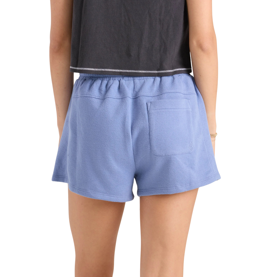 Person wearing blue volcom lived in fleece shorts and a black crop top with graphic design on a white background