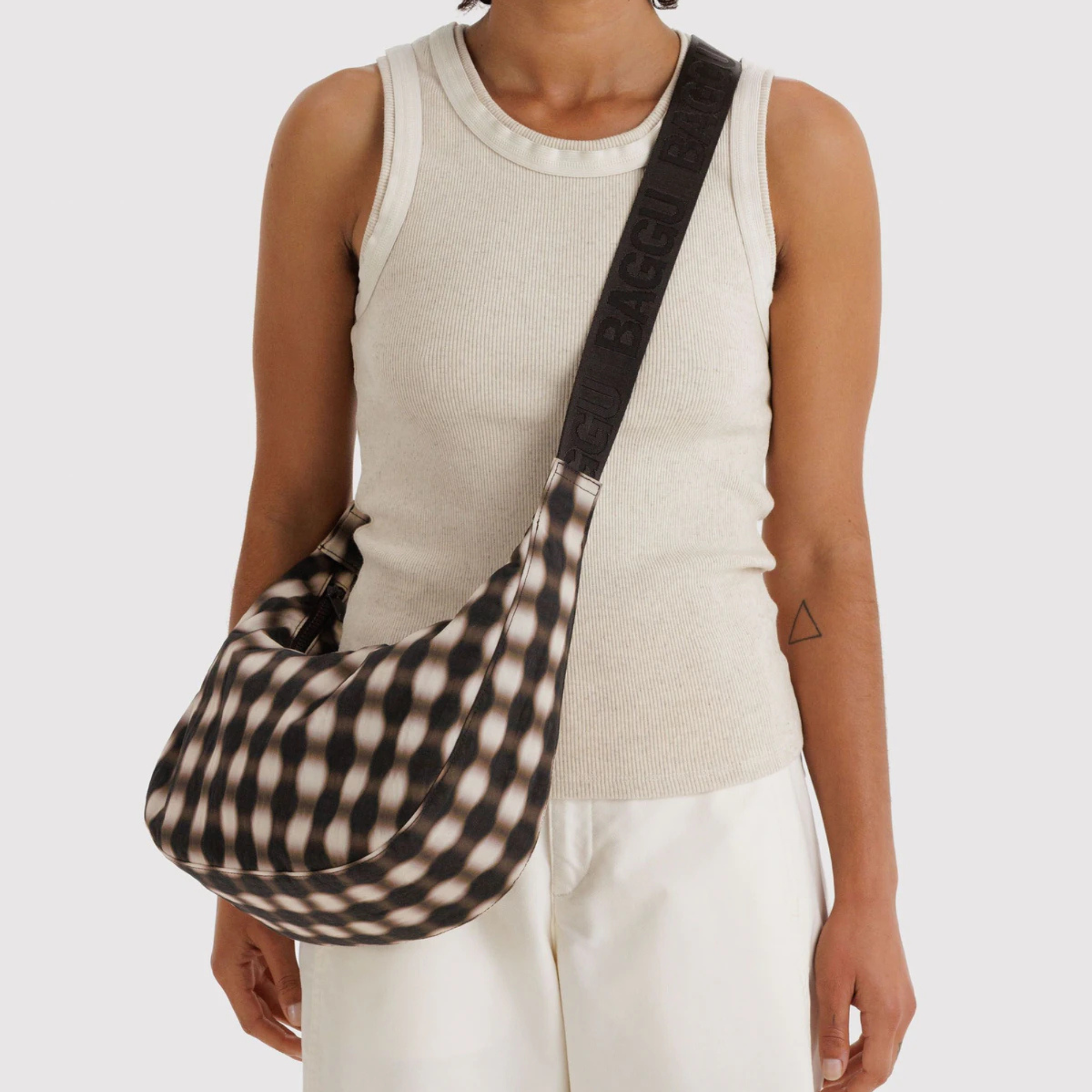 blurred brown and white gingham baggu medium nylon crescent bag on a person