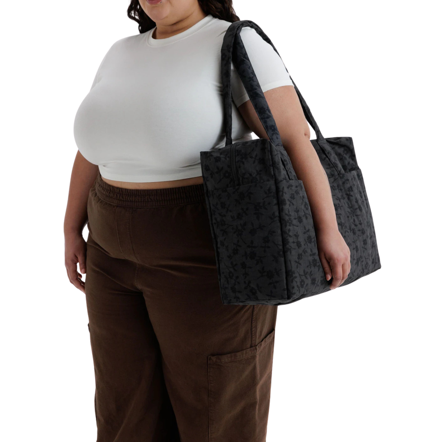 A black baggu cloud carry-on tote bag with a subtle tonal floral pattern, featuring two top handles and side pockets, shown against a plain white background.