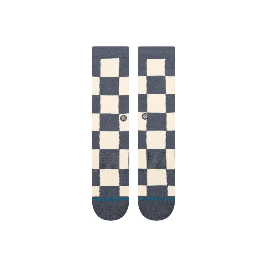 A pair of stance chaturanga crew socks with a blue-gray and cream checkerboard pattern, featuring a small circular Stance logo on the side and a thin teal stripe on the toes.