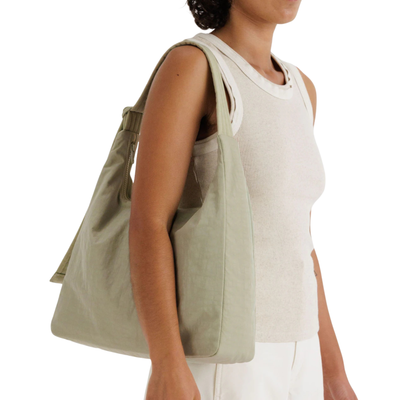 Person holding a light green baggu tote bag on a white background