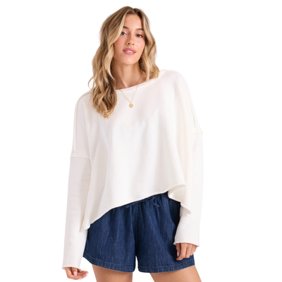 a woman wearing a white volcom gnarly sweatshirt and blue denim shorts on a white background