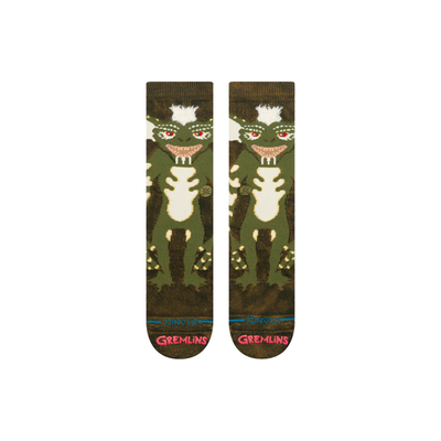 A pair of stance gremlins crew socks featuring a green and brown stripe from gremlins design on the upper leg, red eyes, and 'stance' printed in red on the toes.