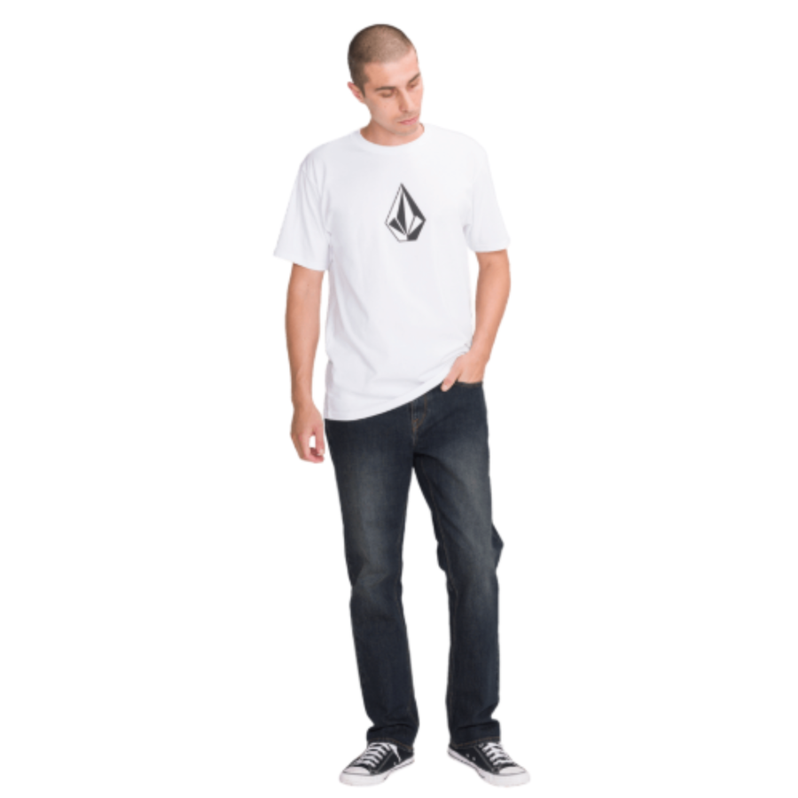 man in a white volcom logo t-shirt wearing dark blue volcom solver denim jeans with black converse all stars on a white background