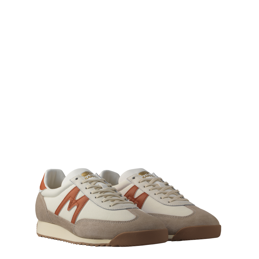 A low-top karhu mestari sneaker in beige suede and off-white leather with a prominent rust-orange 'M' logo on the side, a matching heel tab, and a beige midsole.