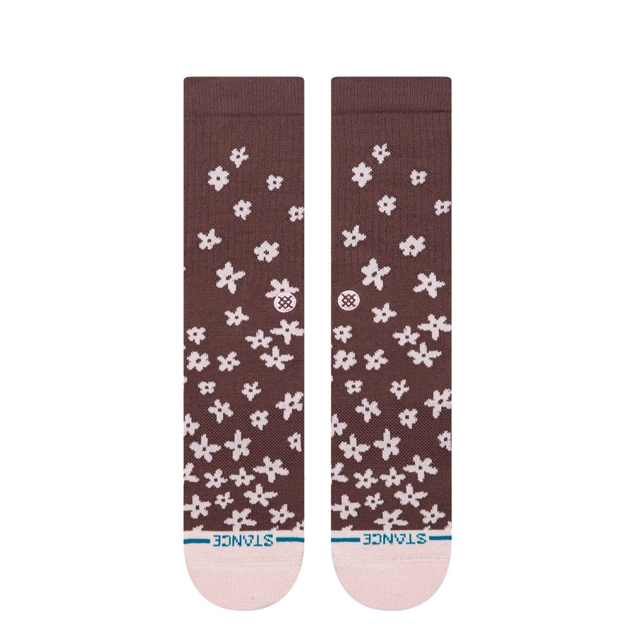 A pair of Stance crew socks in a dark brown color, featuring a white pixelated snowflake pattern and a light pink toe and heel, with the Stance brand logo visible on the side and toe.