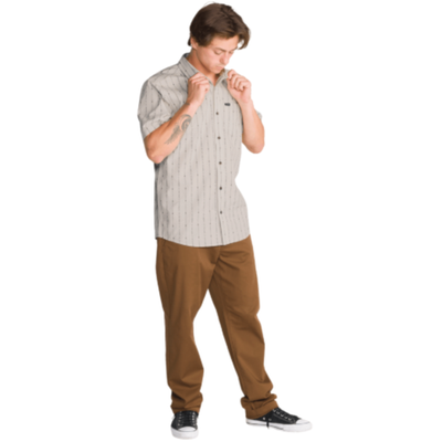 a man wearing an off white volcom bankstone ii short sleeve button-up shirt with vertical pattern with brown pants on a white background