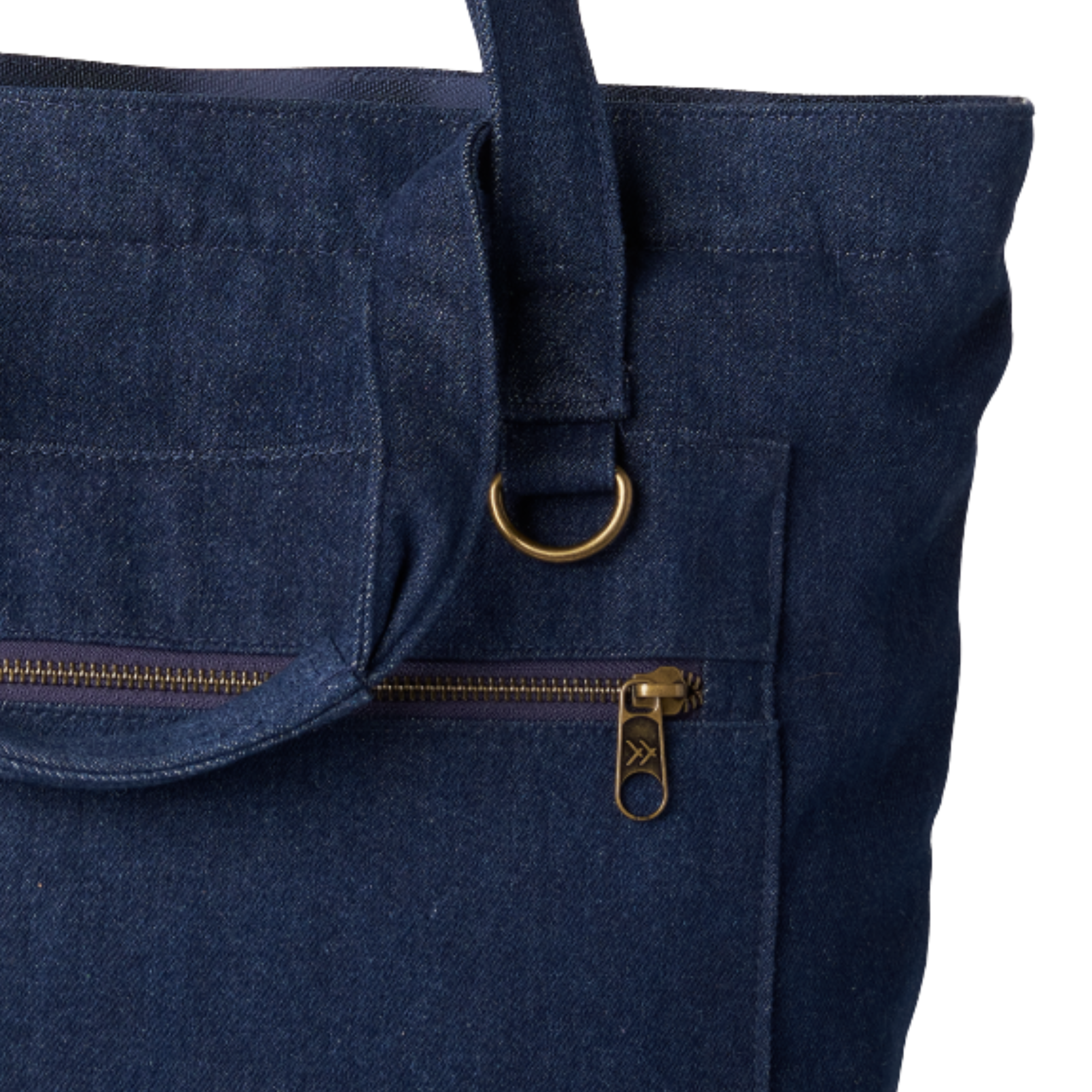Close-up of a dark navy blue canvas tote bag featuring a front zippered pocket with a brass zipper pull and a matching brass D-ring on the strap.