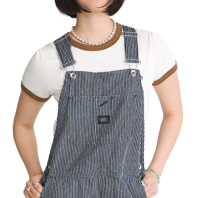 A woman modeling gray and white vans chore stripe vertically striped work overalls over a white t-shirt, standing against a plain white background.