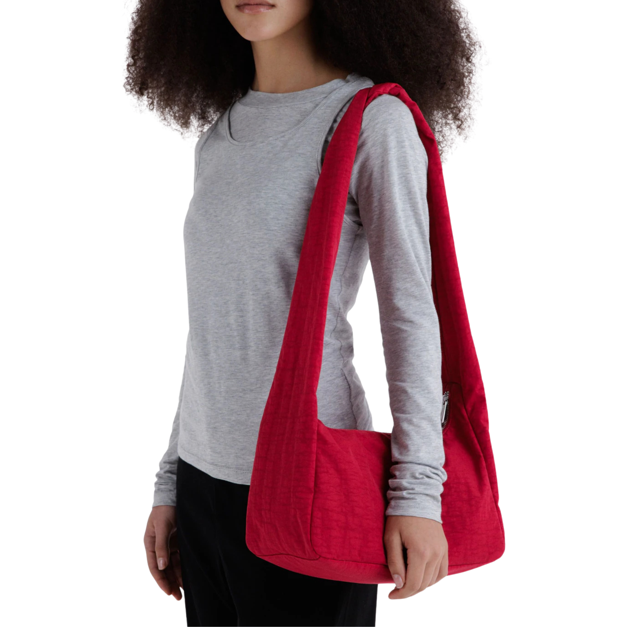 A woman wearing a gray long-sleeve shirt and black pants carries a large, bright red fabric baggu merigue shoulder bag with a single long strap, shown against a plain white background.