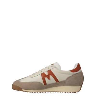 A low-top karhu mestari sneaker in beige suede and off-white leather with a prominent rust-orange 'M' logo on the side, a matching heel tab, and a beige midsole.