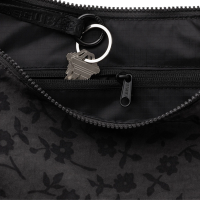 A black crescent-shaped baggu shoulder bag with a subtle tonal floral pattern, featuring a matching black strap with embossed lettering, shown against a plain white background.