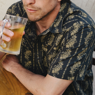 man drinking a beer while wearing a Holwer Brothers H Bar B Snapshirt grampa's curtains in a black with a gold floral design