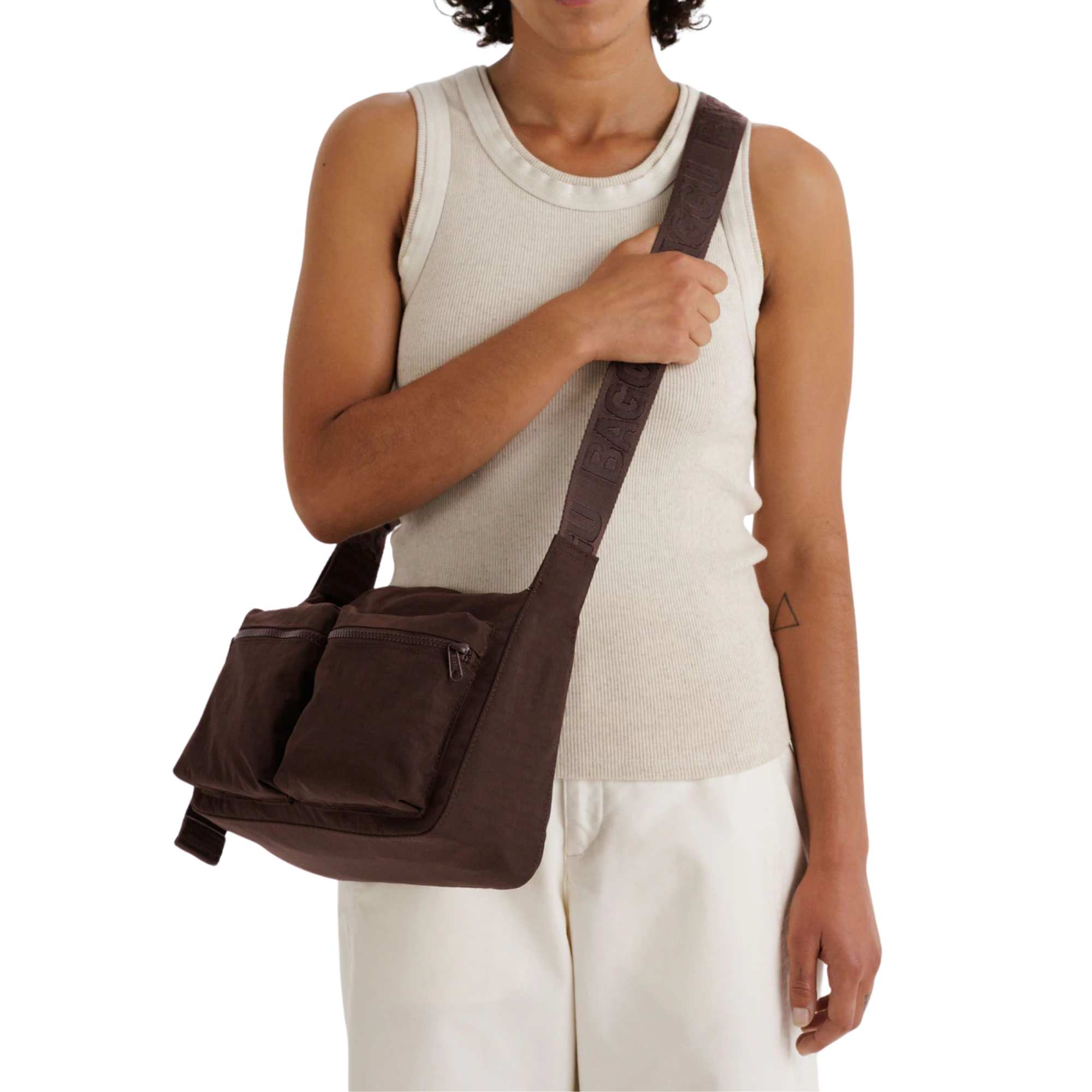 A person wearing a dark brown baggu cargo crossbody bag with dual front zippered pockets and a wide, patterned shoulder strap, shown against a plain white background.