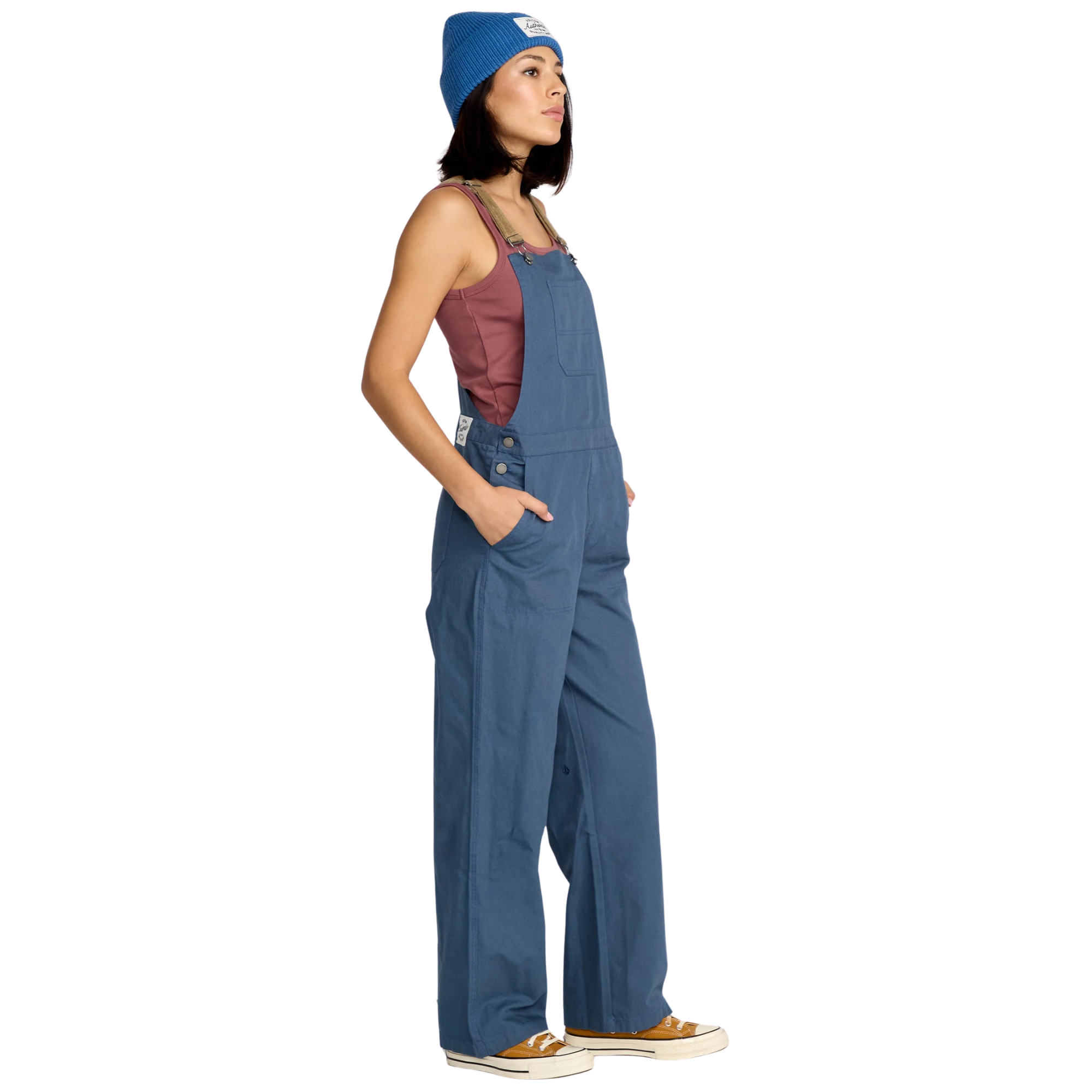 Woman wearing blue volcom full cut overalls with brown cordoroy straps and a matching beanie on a white background