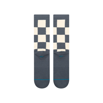 A pair of stance chaturanga crew socks with a blue-gray and cream checkerboard pattern, featuring a small circular Stance logo on the side and a thin teal stripe on the toes.