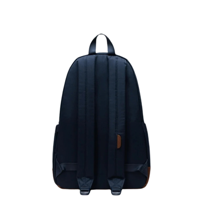 back of a Navy herschel heritage backpack with tan leather bottom and details on a white background